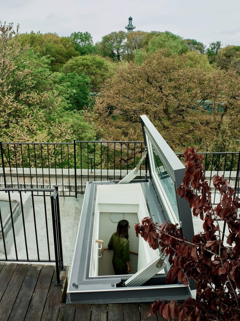 Opening skylight on a roof deck with trees below, woman walking up the stairs
