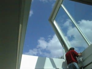 A person installs a custom hinged glass skylight onsite